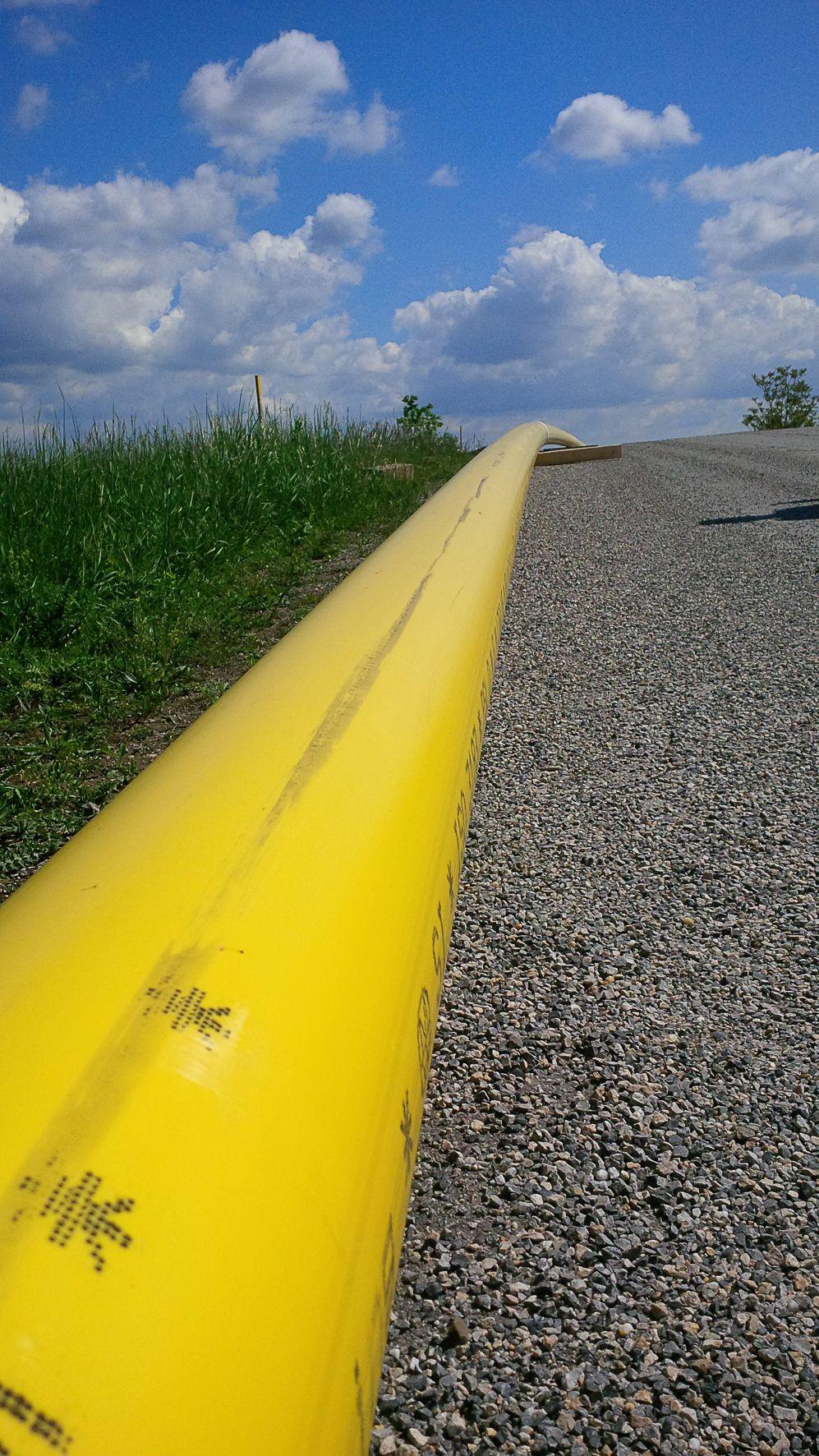 Ein gelbes Erdgasleitungsrohr erstreckt sich entlang einer Kiesstraße mit grünem Gras am Rand.