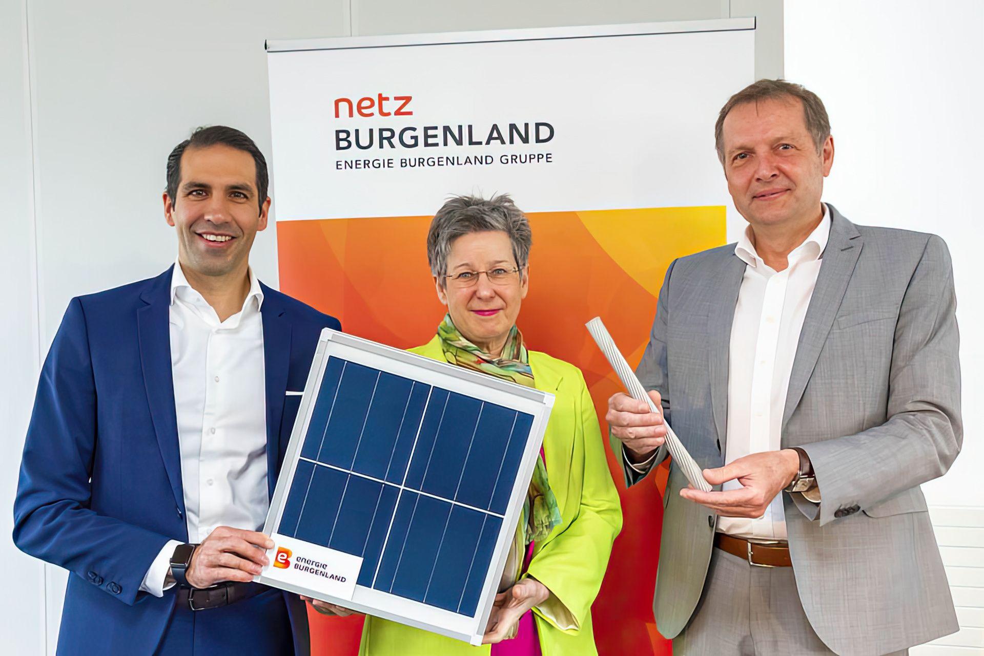 Drei Personen präsentieren stolz eine Solarpanel und Energiekabel, symbolisch für erneuerbare Energien.